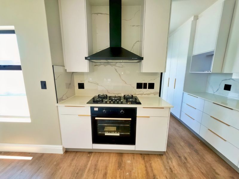 Modern kitchen featuring sleek white cabinetry, stone countertops, marble-look splashback, and high-quality built-in gas hob and oven.