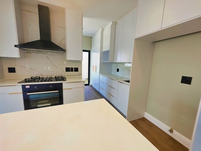 Modern kitchen featuring sleek white cabinetry, stone countertops, marble-look splashback, and integrated gas hob with extractor fan.
