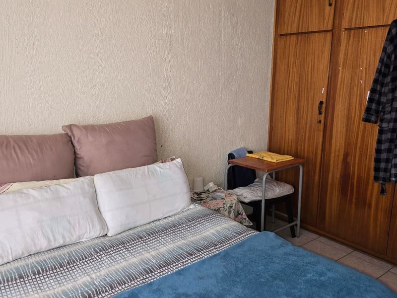 A bedroom featuring built-in wooden wardrobes and tiled flooring, offering a functional space with potential for modern updates.