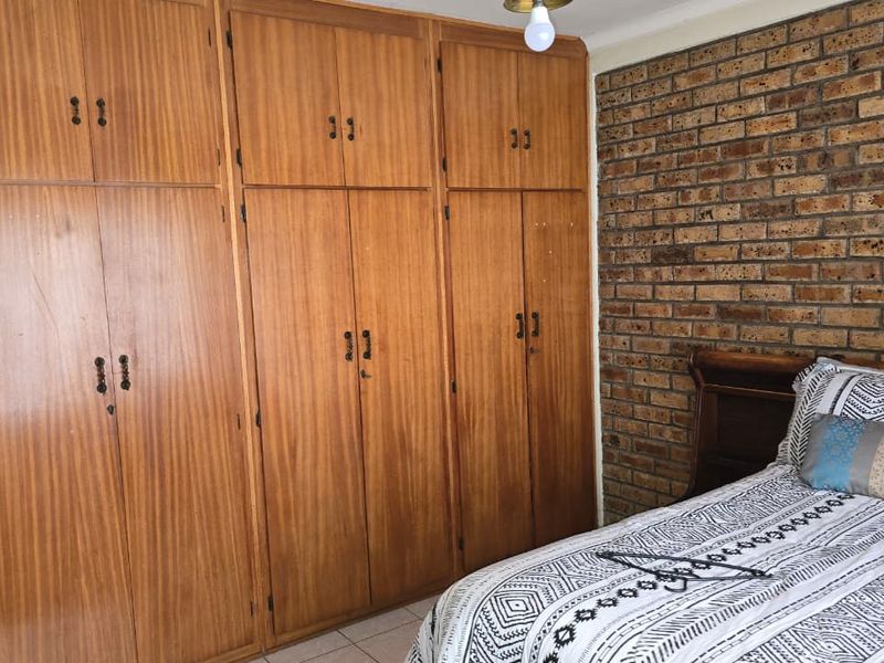 A bedroom featuring a prominent exposed brick wall and extensive built-in wooden cabinetry, offering ample storage space with a classic, dated aesthetic.