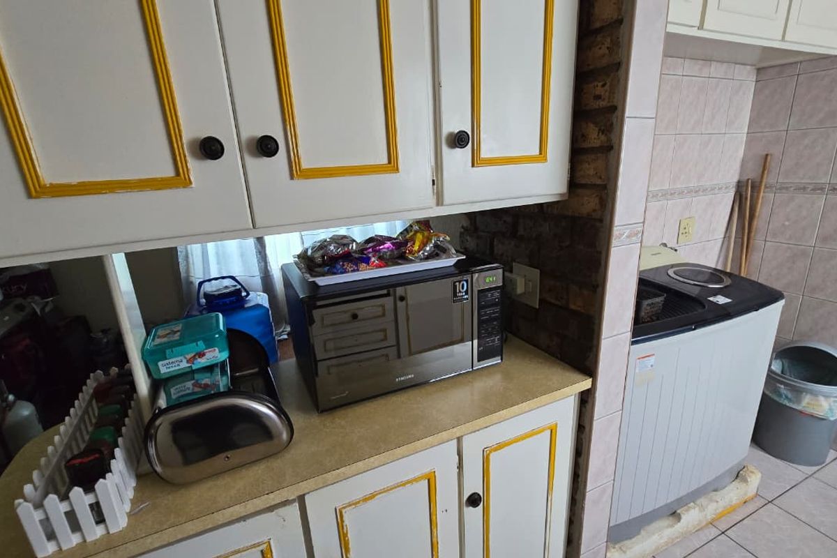 A functional kitchen area featuring built-in cabinetry with decorative trim, laminate countertops, and exposed brick accents, requiring cosmetic updates to modernize the space.