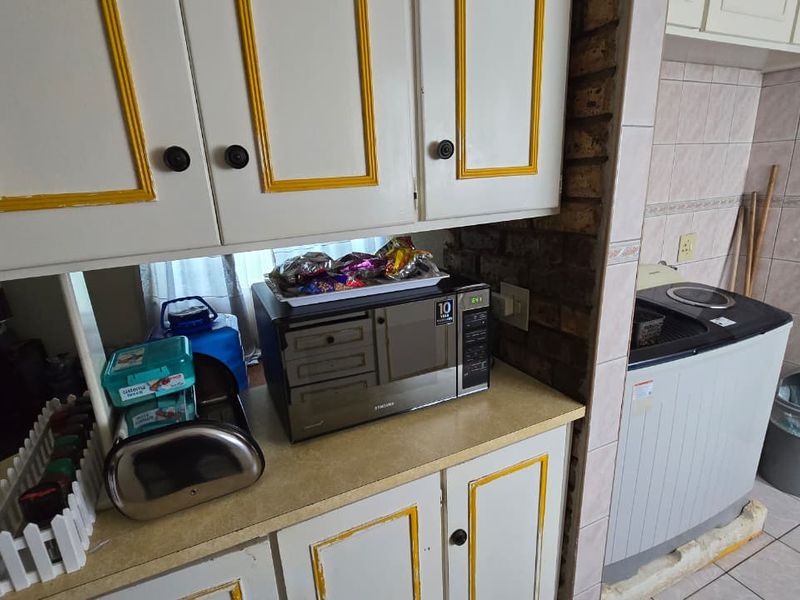 A functional kitchen area featuring built-in cabinetry with decorative trim, laminate countertops, and exposed brick accents, requiring cosmetic updates to modernize the space.