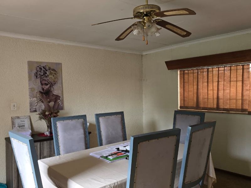 A functional dining room featuring a ceiling fan, textured walls, and vertical window blinds, offering a neutral space ready for personalization.