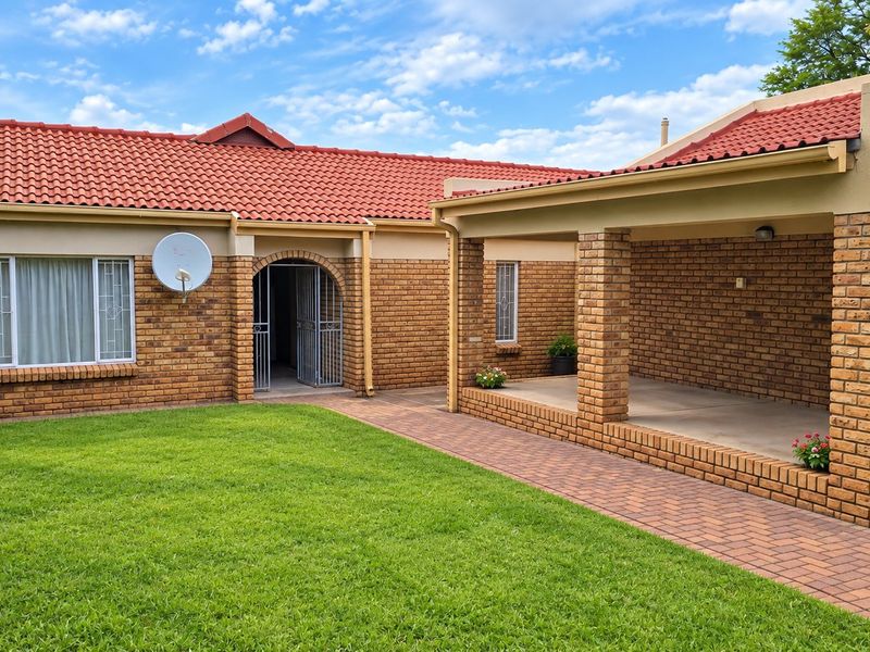 A well-maintained rear exterior view featuring a face brick facade, terracotta roof tiles, and a spacious covered patio overlooking a neat lawn.