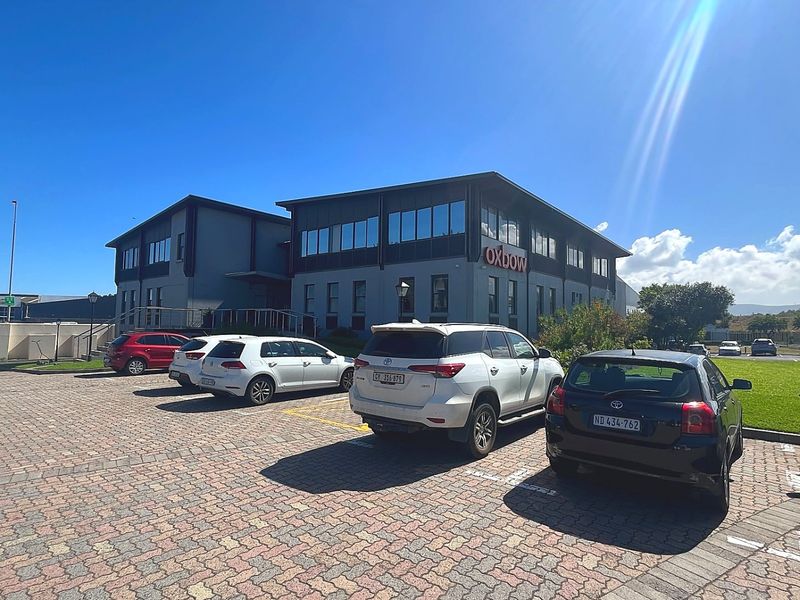 Front view of a multi-story commercial office building featuring a paved parking area and modern exterior facade.