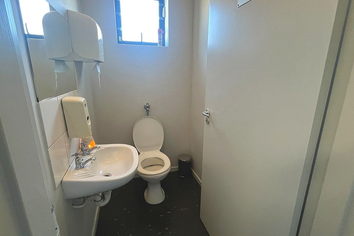 A functional commercial restroom featuring a wall-mounted basin, toilet, and tiled splashback, providing essential facilities for staff or clients.