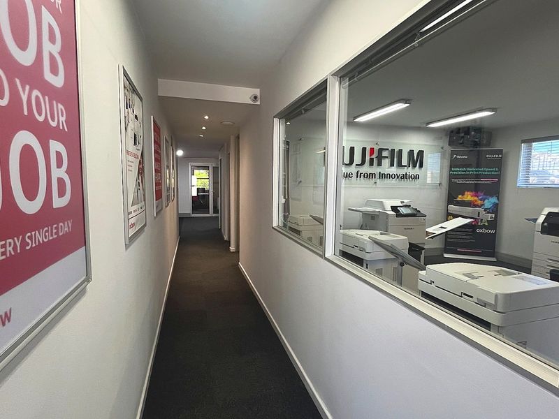 A clean commercial hallway featuring recessed lighting, carpeted flooring, and a large glass partition wall looking into an office space.