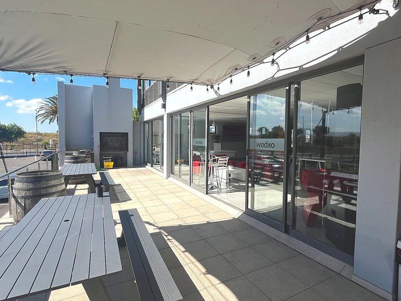 A spacious covered outdoor patio featuring tiled flooring, a built-in braai, and large sliding glass doors providing seamless access to the interior commercial space.