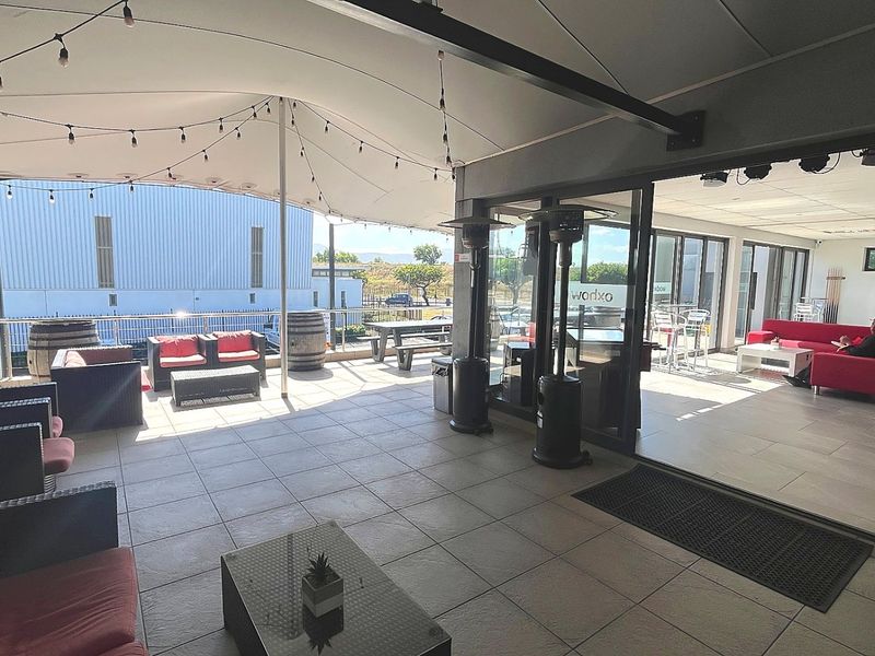 A spacious covered patio area featuring tiled flooring, a tensioned fabric canopy, and large sliding glass doors connecting to the interior commercial space.