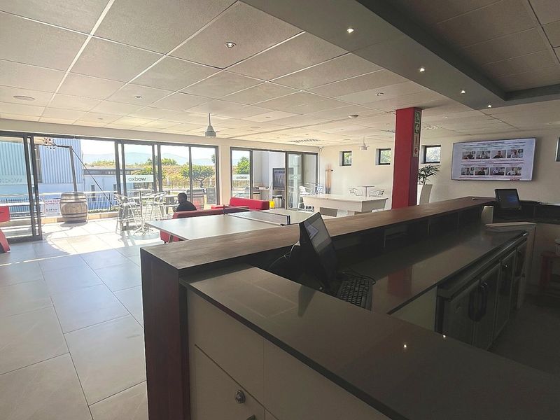 Spacious commercial clubhouse area featuring a built-in bar counter, modern tiled flooring, recessed ceiling lighting, and large sliding glass doors opening to an outdoor patio.