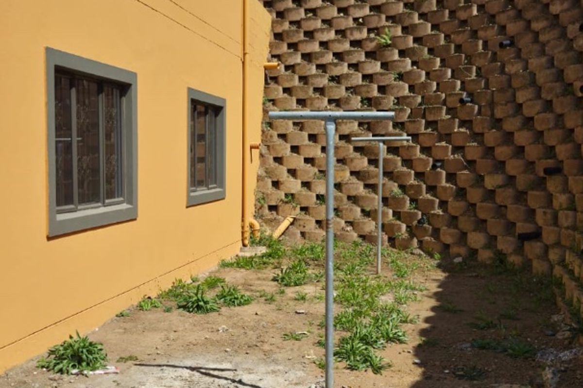 Rear exterior area featuring a large concrete block retaining wall, metal washing lines, and an unpaved ground surface requiring landscaping.