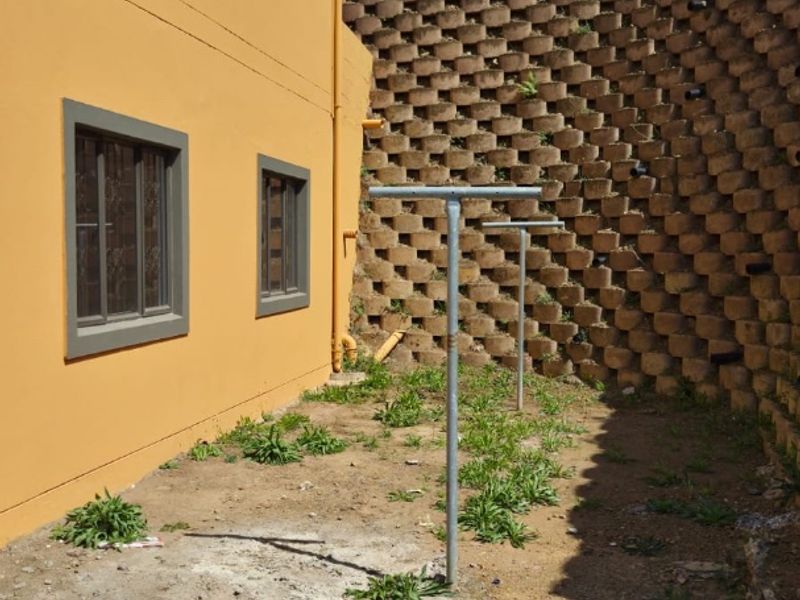 Rear exterior area featuring a large concrete block retaining wall, metal washing lines, and an unpaved ground surface requiring landscaping.