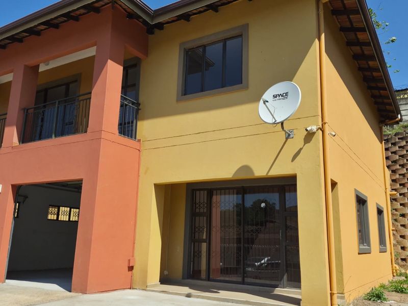 A two-story residential property featuring a garage, balcony, and sliding glass doors with security gates, set against a landscaped retaining wall.