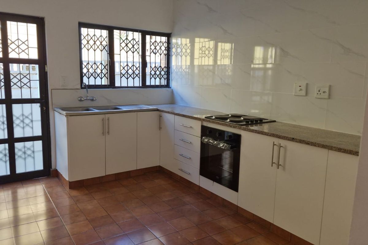 A clean, functional kitchen featuring white cabinetry, granite countertops, a built-in oven and hob, and tiled splashbacks with secure window and door access.