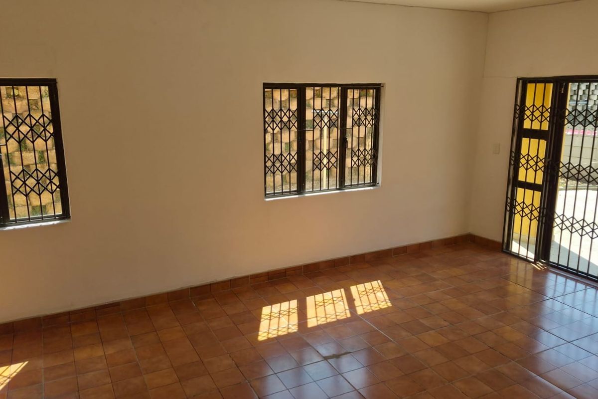 An empty living room featuring tiled flooring, security bars on the windows, and a security gate leading to the exterior.