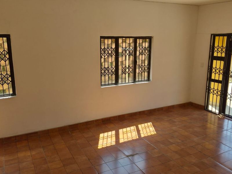 An empty living room featuring tiled flooring, security bars on the windows, and a security gate leading to the exterior.