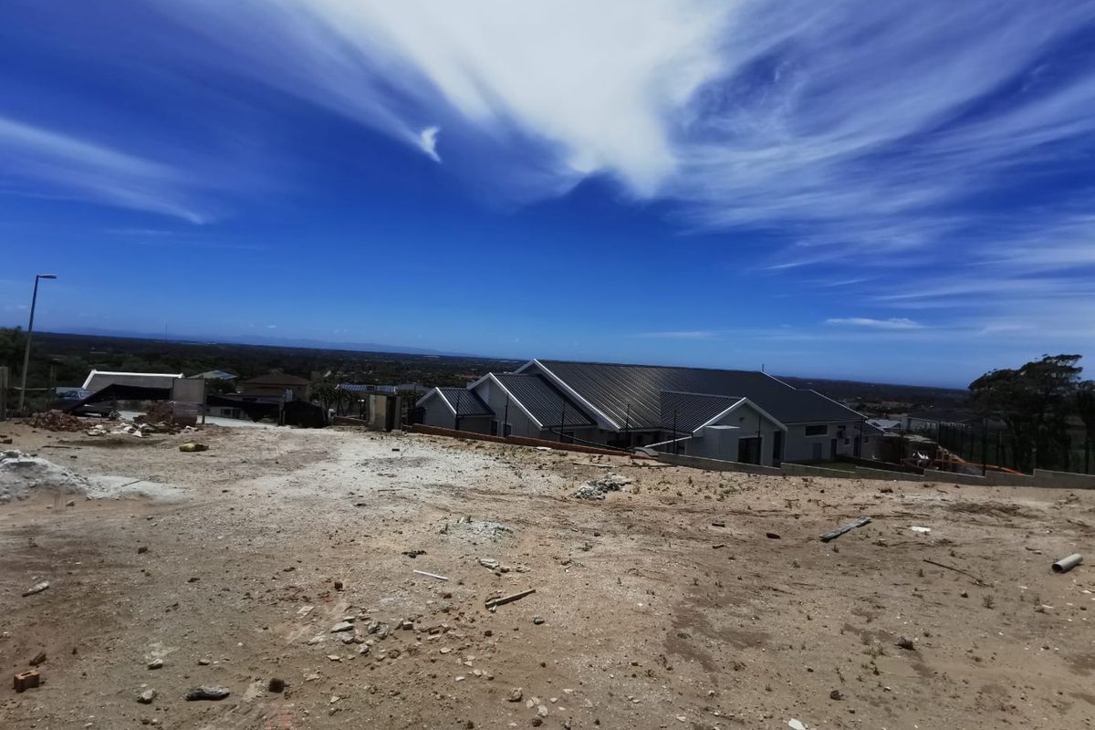 A view of a vacant residential plot with construction debris, overlooking neighboring properties and the surrounding landscape.