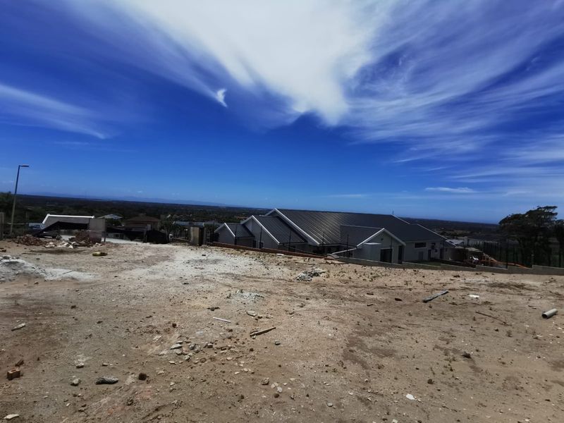 A view of a vacant residential plot with construction debris, overlooking neighboring properties and the surrounding landscape.