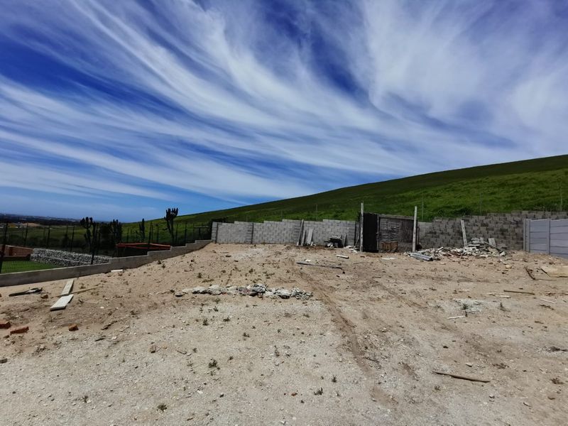 Vacant residential land featuring a concrete block boundary wall, wire mesh fencing, and a gabion retaining wall, with construction debris present on site.
