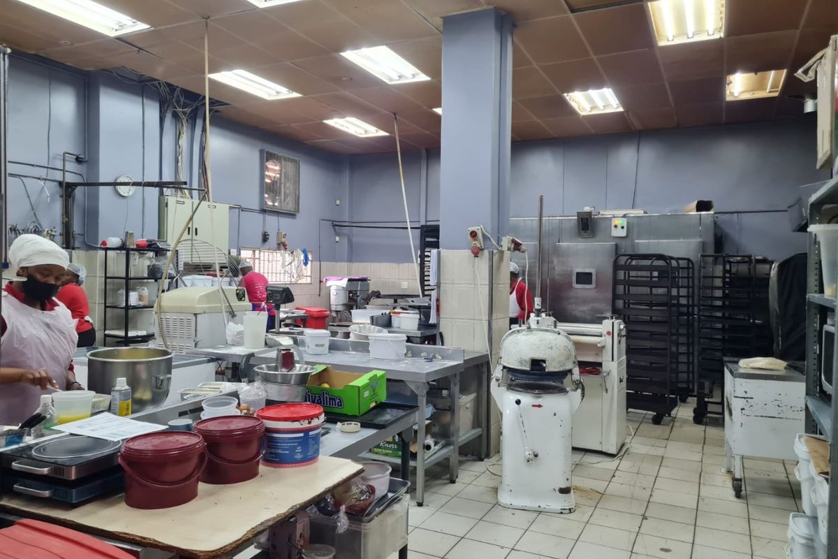 A functional commercial kitchen space featuring stainless steel work surfaces, industrial baking equipment, tiled flooring, and suspended ceiling lighting.