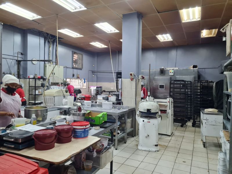 A functional commercial kitchen space featuring stainless steel work surfaces, industrial baking equipment, tiled flooring, and suspended ceiling lighting.
