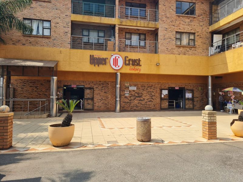 Front facade of a commercial building featuring face brick construction, metal balcony railings, and a paved entrance area with prominent commercial signage.