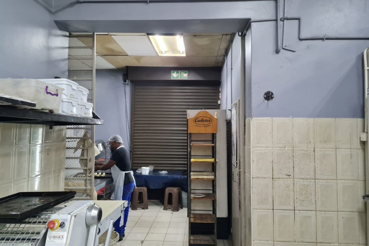 Commercial kitchen area featuring tiled surfaces, exposed conduit piping, and a secure roller shutter door access point.