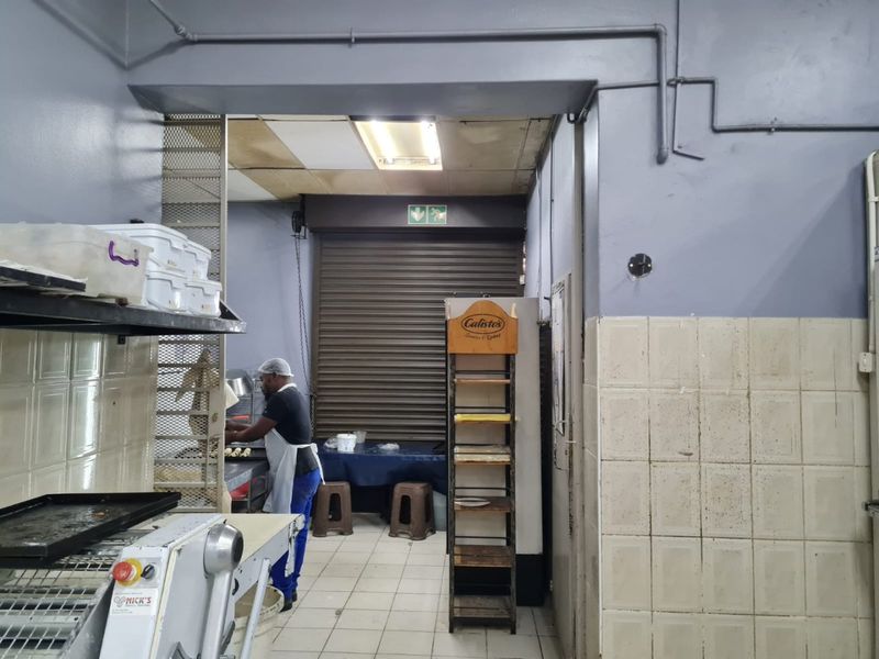 Commercial kitchen area featuring tiled surfaces, exposed conduit piping, and a secure roller shutter door access point.