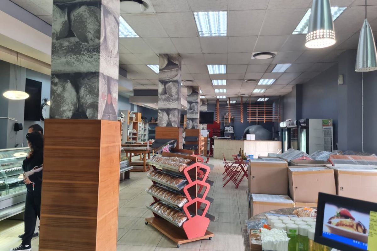 Spacious commercial open-plan retail area featuring tiled flooring, structural columns, and a service counter, suitable for a bakery or cafe setup.