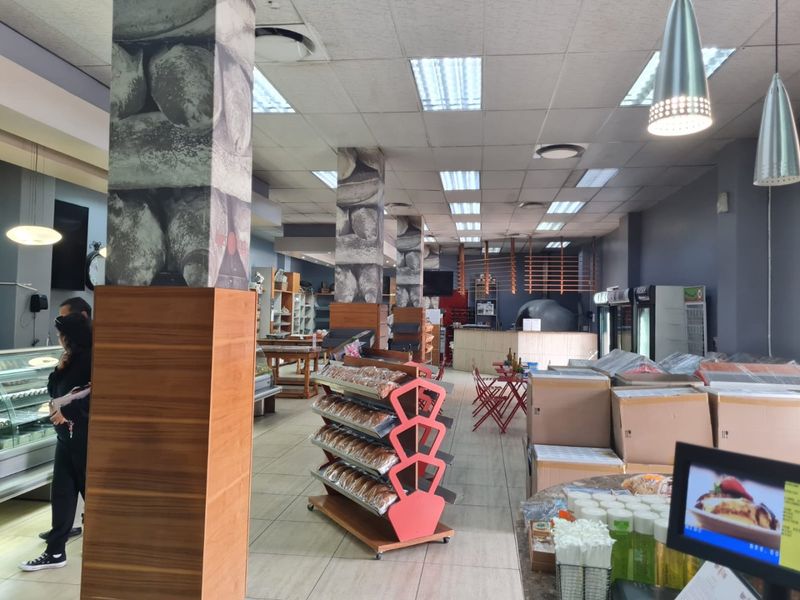 Spacious commercial open-plan retail area featuring tiled flooring, structural columns, and a service counter, suitable for a bakery or cafe setup.