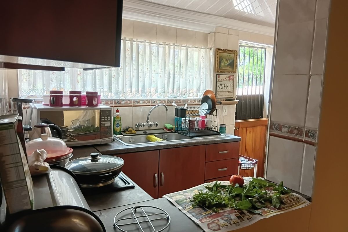 A functional kitchen featuring built-in cabinetry, a stainless steel sink with mixer tap, and tiled backsplash, offering a practical layout for daily meal preparation.