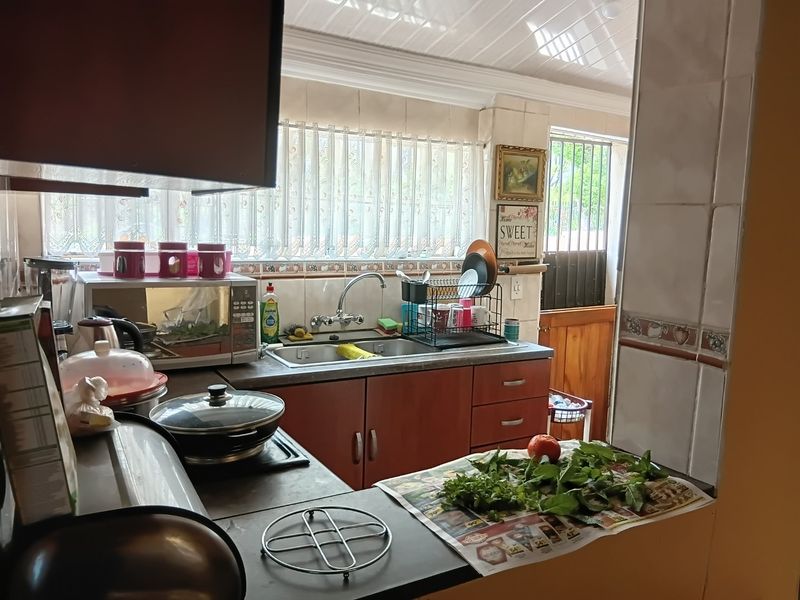 A functional kitchen featuring built-in cabinetry, a stainless steel sink with mixer tap, and tiled backsplash, offering a practical layout for daily meal preparation.
