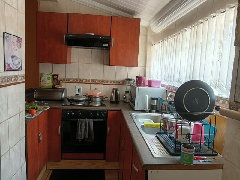A functional kitchen featuring wood-finish cabinetry, tiled backsplash, built-in oven with extractor fan, and a stainless steel sink with ample counter space.
