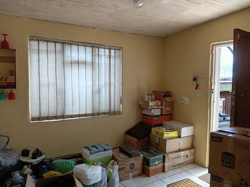 A basic living area featuring tiled flooring, vertical blinds, and a timber ceiling, currently used for storage.
