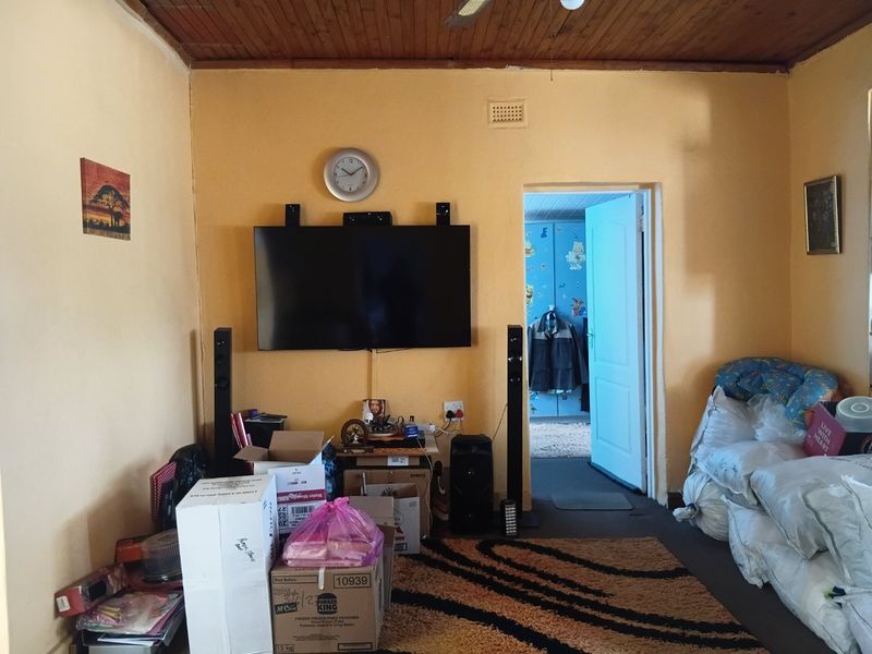 A living room featuring a timber-paneled ceiling and yellow walls, with an internal doorway leading to an adjacent bedroom.