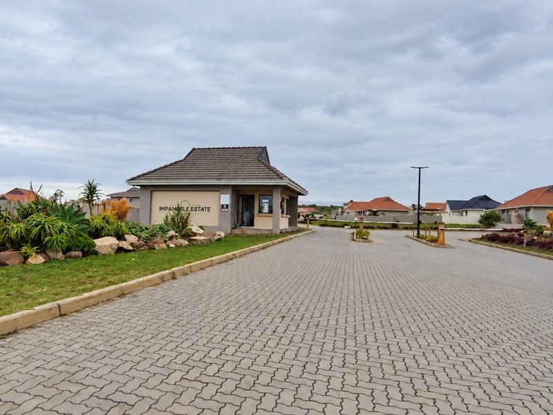 The entrance to Impangele Estate featuring a well-maintained security gatehouse, paved driveway, and landscaped garden areas.