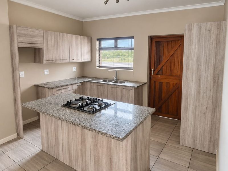 Modern kitchen featuring light wood-grain cabinetry, granite countertops, a central island with a gas hob, and tiled flooring.