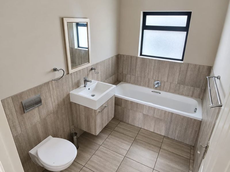 A modern, well-maintained bathroom featuring a wall-hung toilet, vanity basin, and a built-in bathtub with neutral floor-to-ceiling tiling.