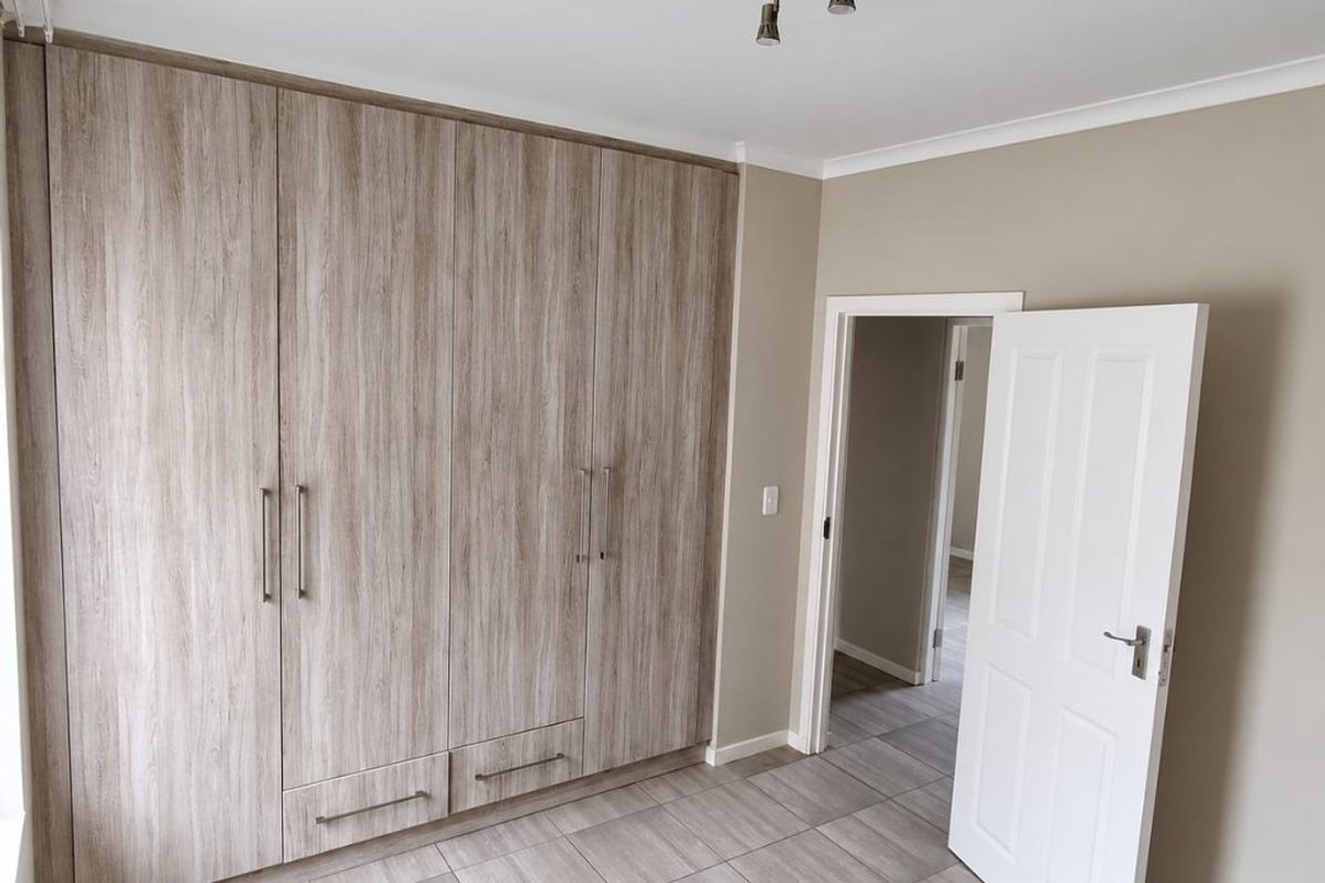 A clean, empty bedroom featuring modern wood-look built-in cupboards, neutral wall tones, and durable tiled flooring.
