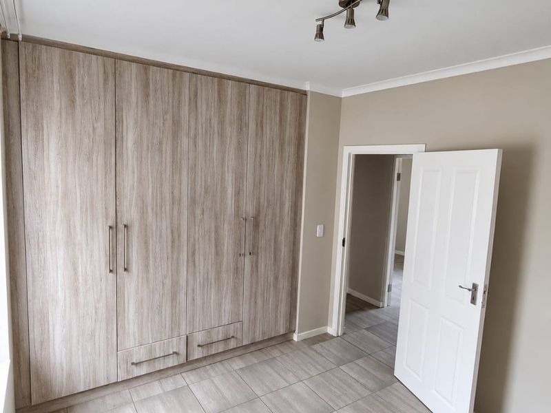 A clean, empty bedroom featuring modern wood-look built-in cupboards, neutral wall tones, and durable tiled flooring.