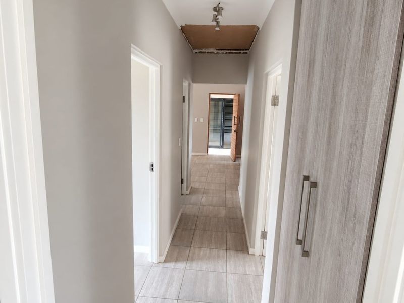 A hallway featuring tiled flooring and built-in cupboards, currently requiring minor ceiling repairs.