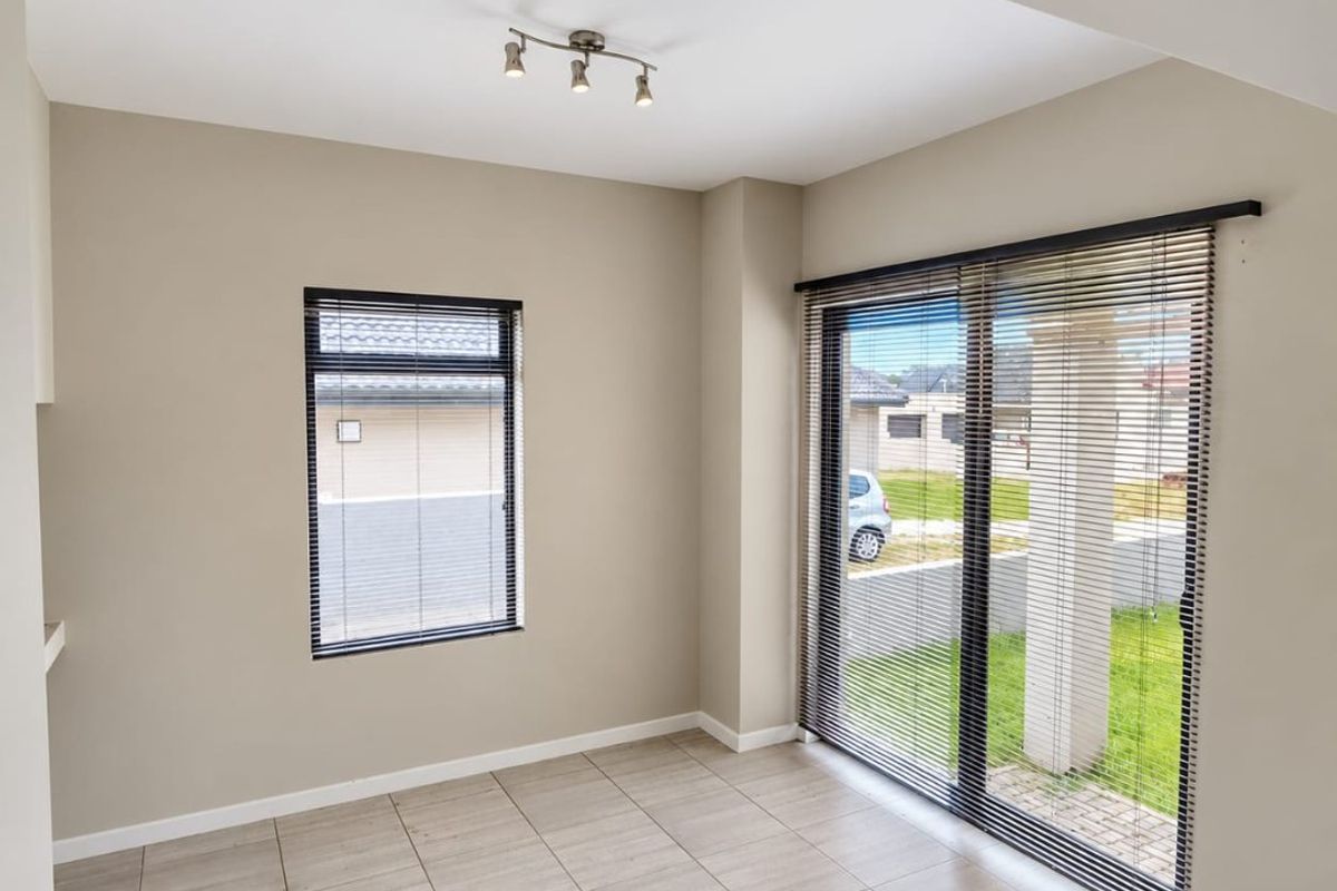 A bright, empty living area featuring neutral tiled flooring, modern spotlight lighting, and large sliding glass doors with fitted venetian blinds.
