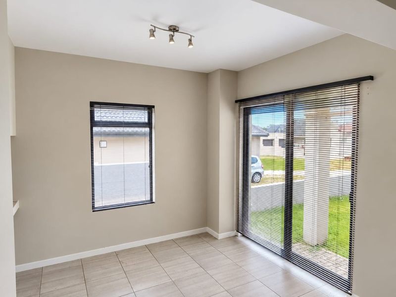 A bright, empty living area featuring neutral tiled flooring, modern spotlight lighting, and large sliding glass doors with fitted venetian blinds.