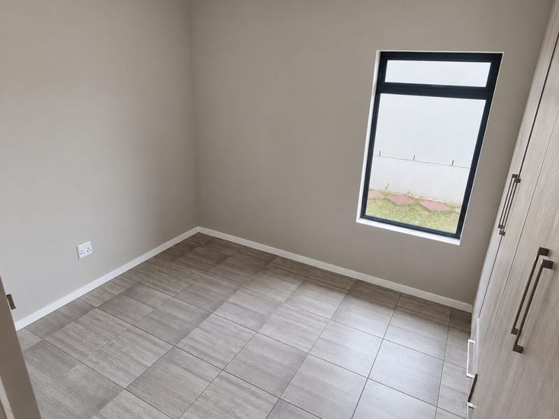 A clean, empty bedroom featuring neutral wall paint, modern tiled flooring, and built-in cupboards with a view of the exterior.