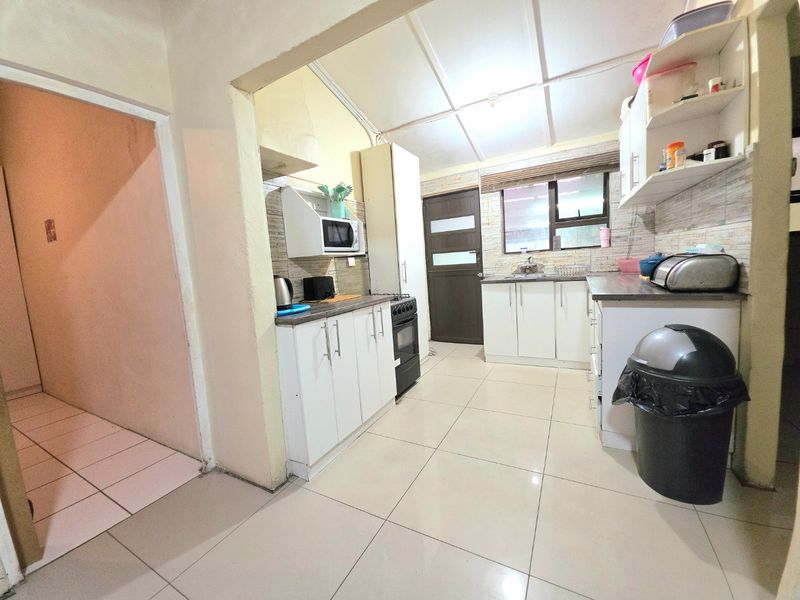 Functional kitchen featuring white cabinetry, laminate countertops, tiled backsplash, and tiled flooring, providing a practical workspace with direct access to adjacent areas.