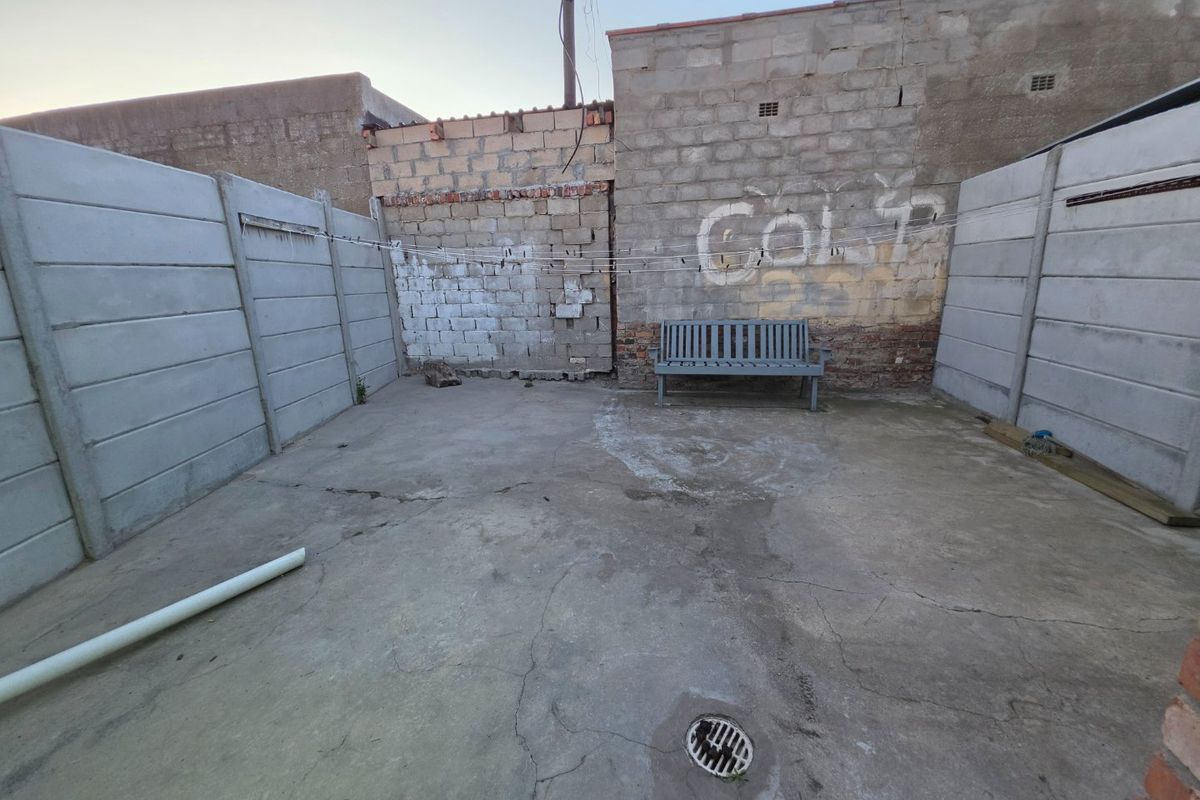 A rear courtyard area featuring concrete paving, boundary walls, and a drainage point, currently requiring maintenance and cosmetic improvements.