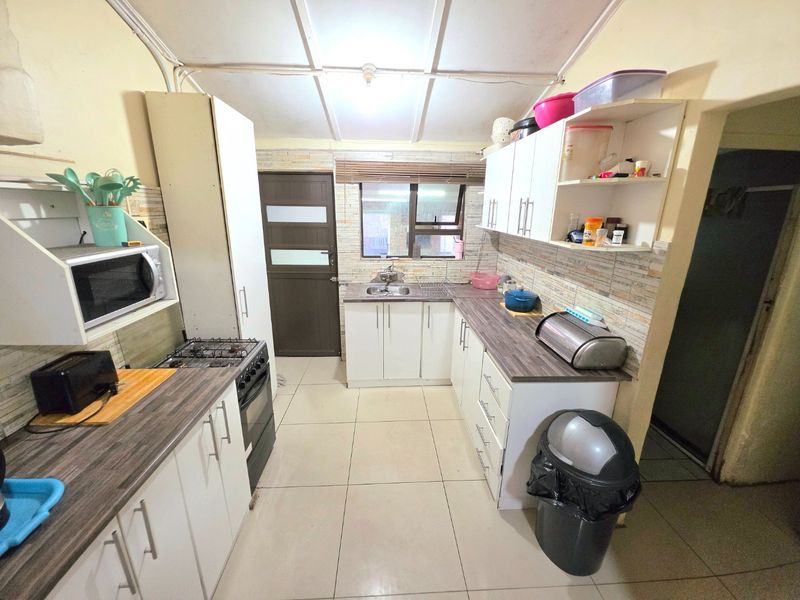 Functional kitchen featuring white cabinetry, laminate countertops, tiled backsplash, and gas stove, with direct access to an exterior door.