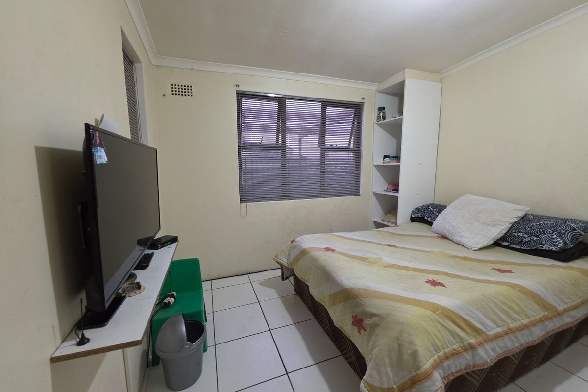 A functional bedroom featuring tiled flooring, a built-in shelving unit, and an aluminium window with venetian blinds.