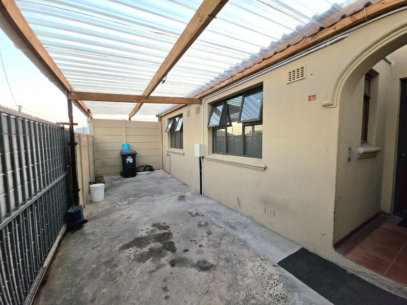 A covered outdoor patio area featuring a translucent roof, concrete flooring, and access to the main building entrance.