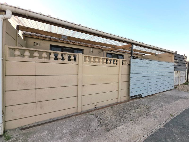 Front exterior view featuring a precast concrete boundary wall, a covered carport area, and a sliding gate entrance.